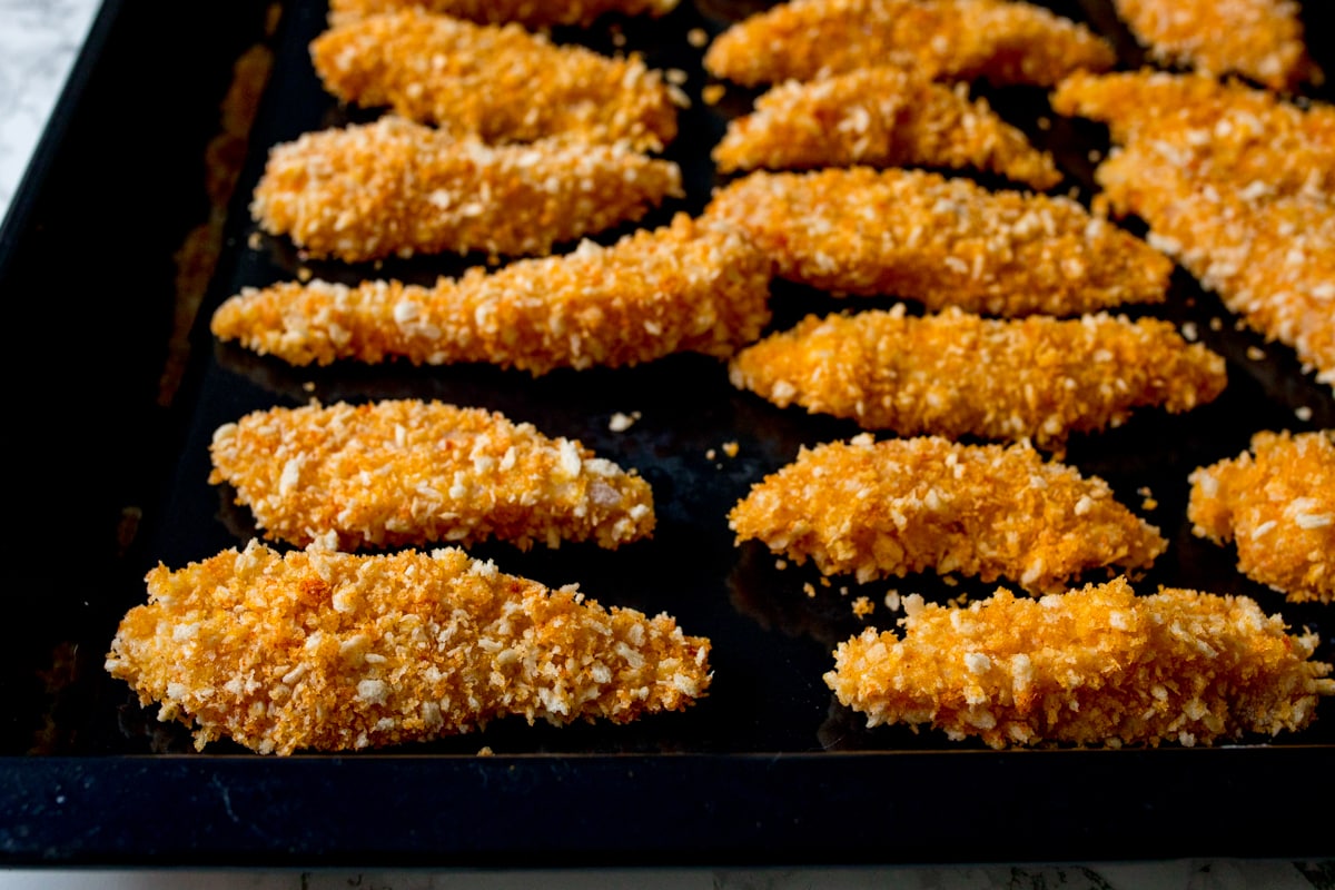 Strips of breaded chicken on a baking tray.