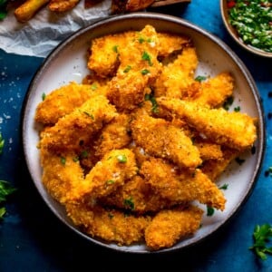 Overhead photo of a bowl full of crispy baked chicken goujons on a blue background.