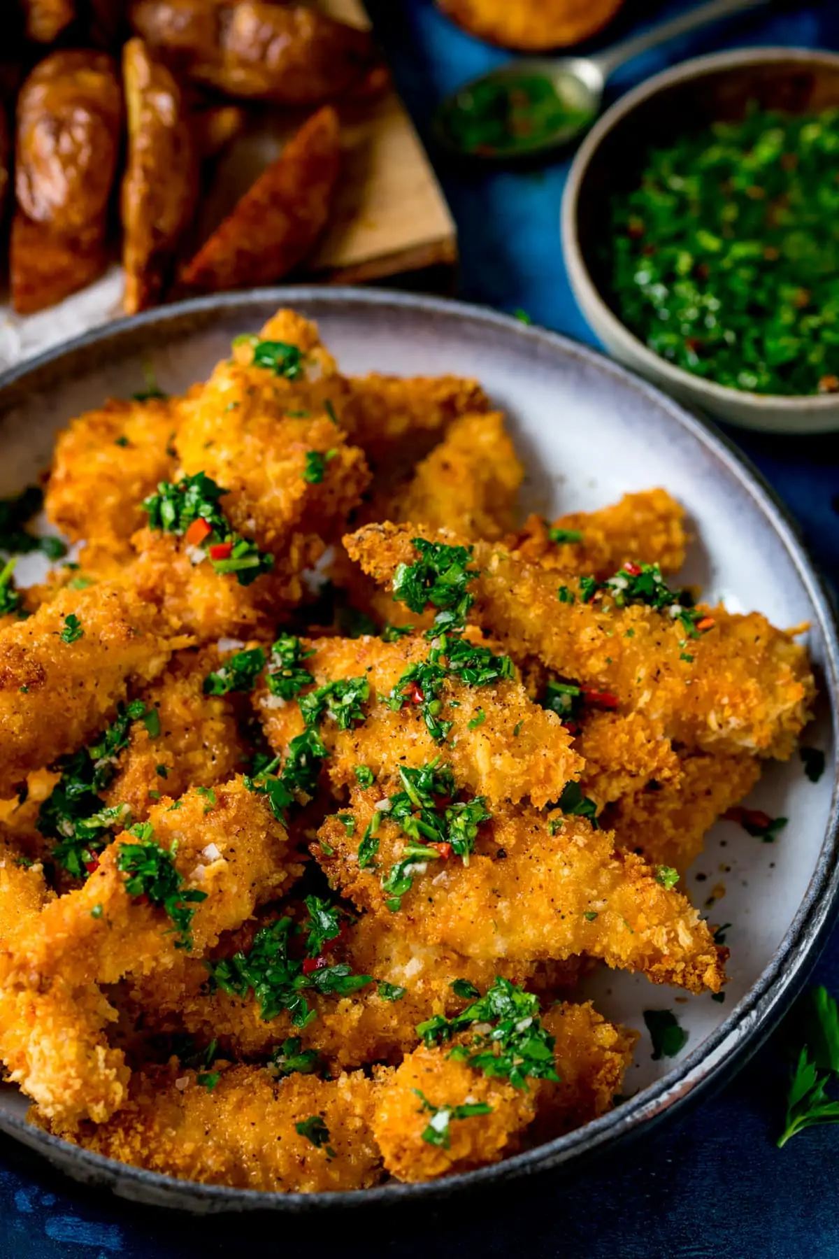 A bowl of golden baked chicken goujons with chimichurri sauce drizzled over.