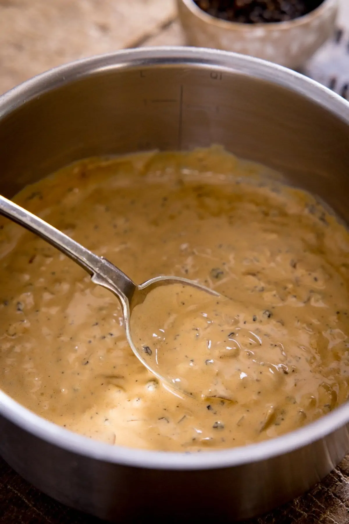 A tall image of a pan of peppercorn sauce being stirred with a metal spoon