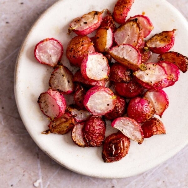 Square image of halved roasted radishes on a white plate, on a light background.