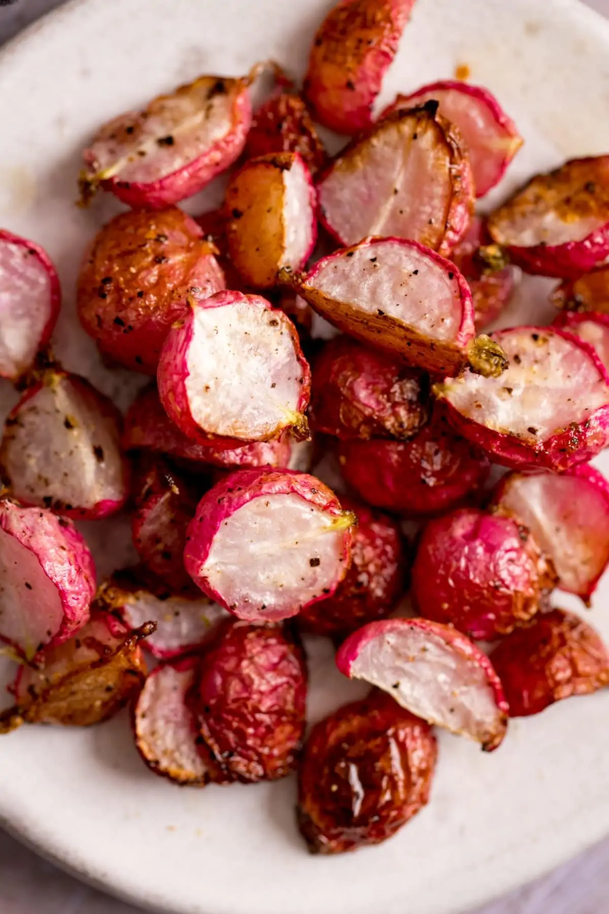 Overhead image of halved roasted radishes on a white plate.