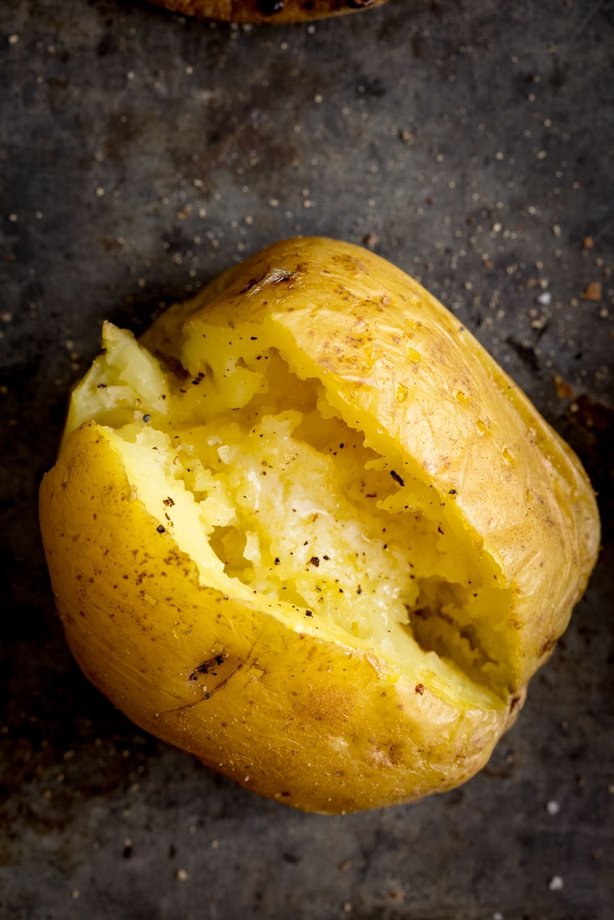 Overhead image of an open jacket potato on a dark metal background. Potato was cooked using method 6 of my baked potato experiment.