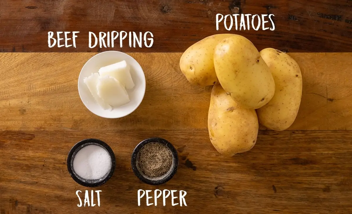 Overhead photo of some large jacket potatoes, beef dripping, salt and pepper on a wooden background.