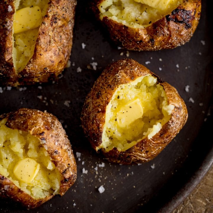 Square overhead image of four open baked potatoes, with butter, on a tray.