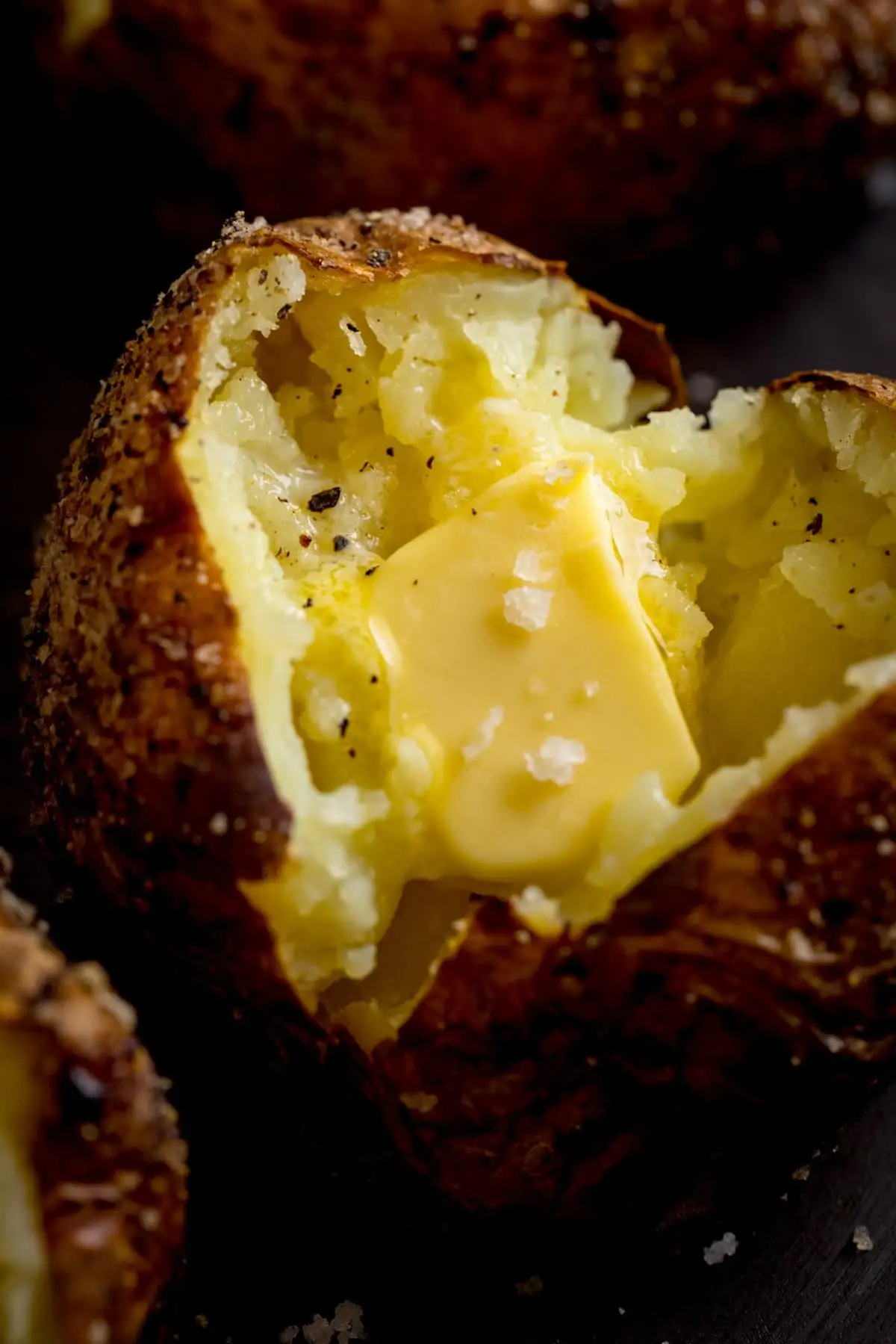 Close up image of an open baked potato, filled with a knob of butter.