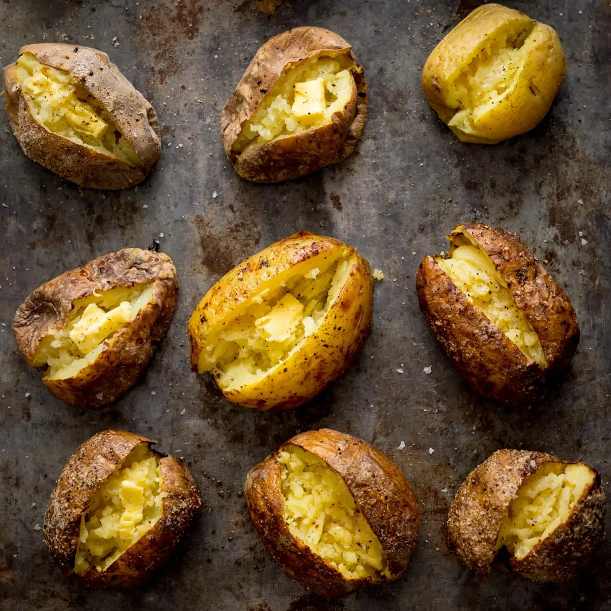 Square image showing 9 baked potatoes on a metal tray.
