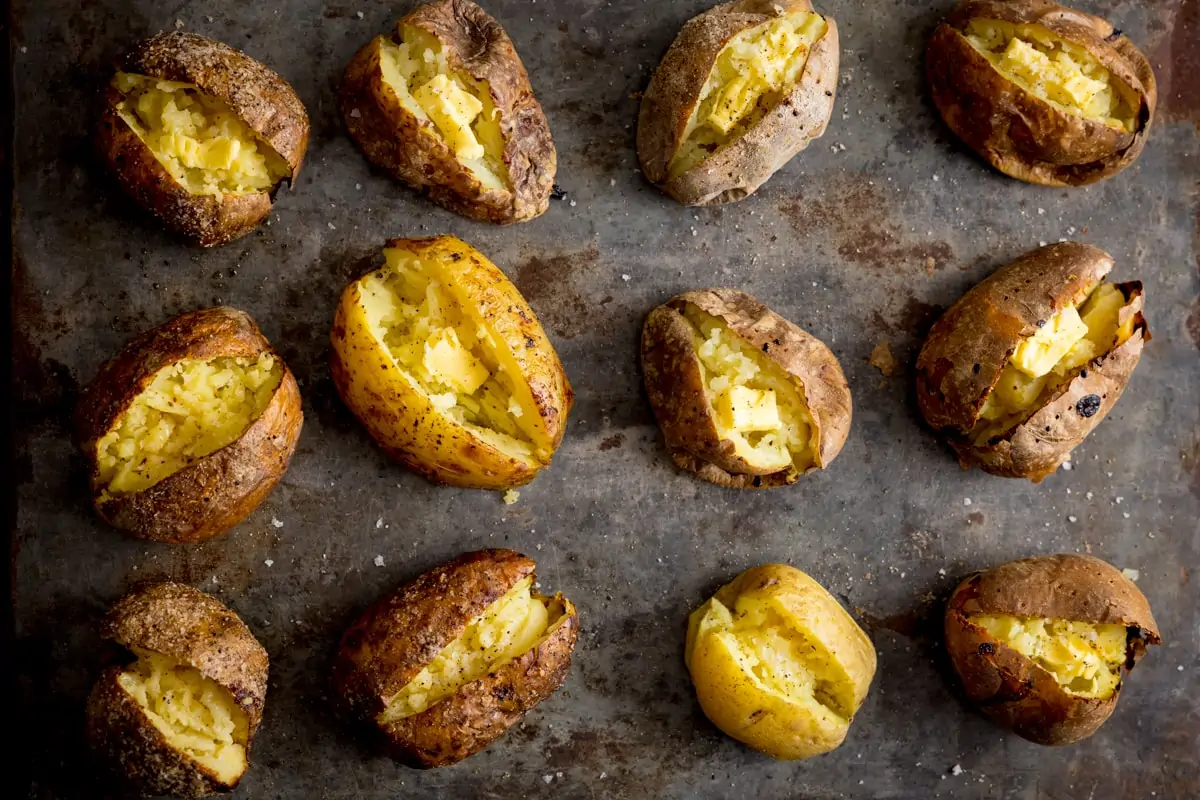 Wide overhead image showing 12 open baked potatoes on a metal tray
