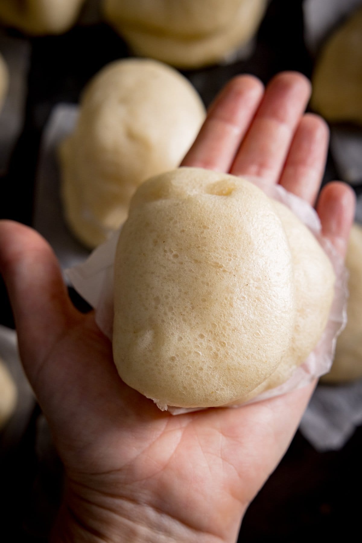 An open hand showing the dough for bao buns, more in the back ground