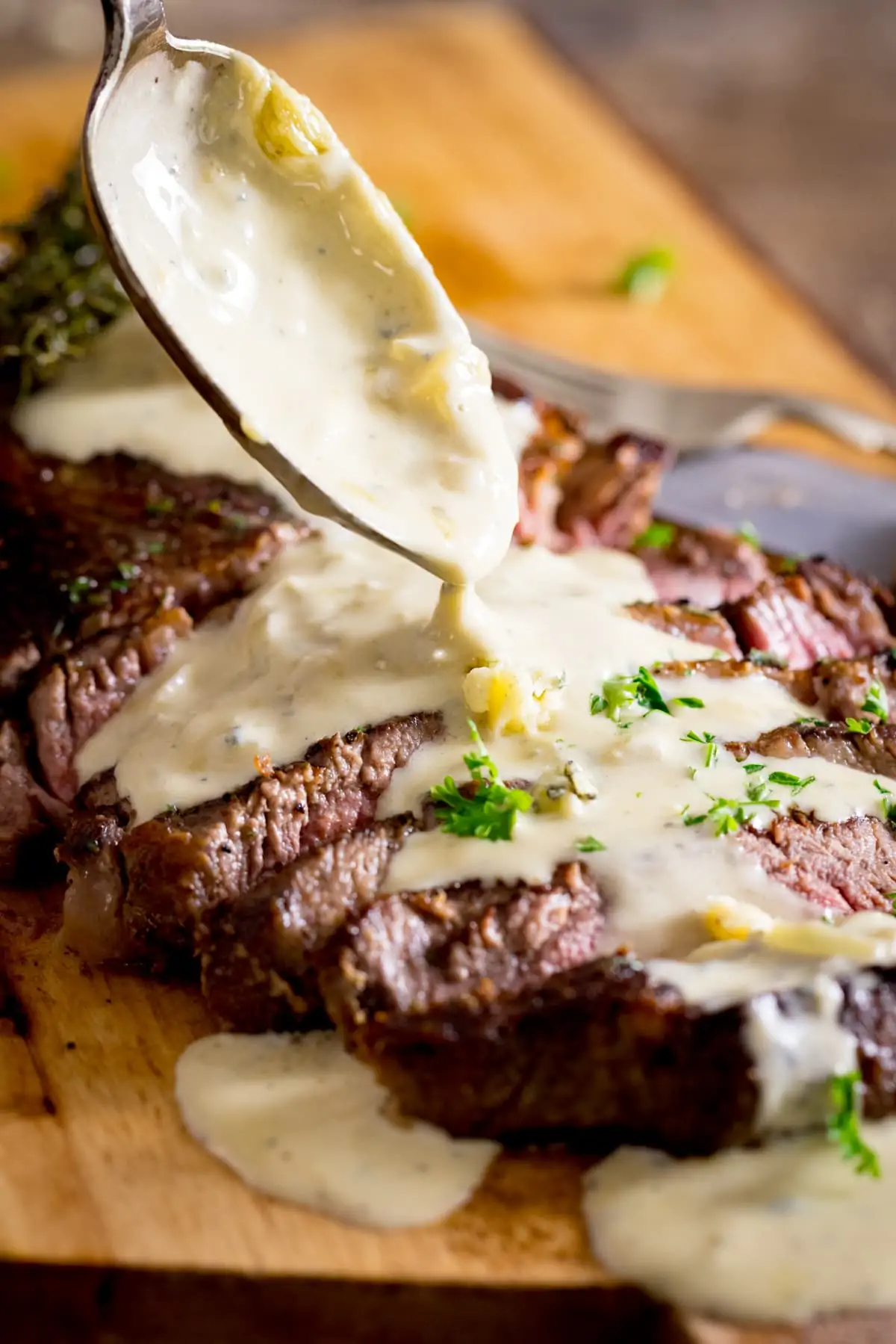 A steak with a blue cheese sauce being poured over it from a spoon