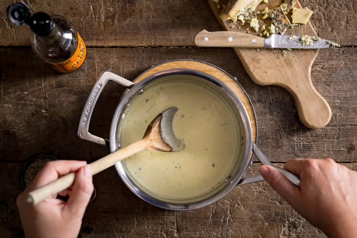 A pan of blue cheese sauce being stirred with a wooden spoon