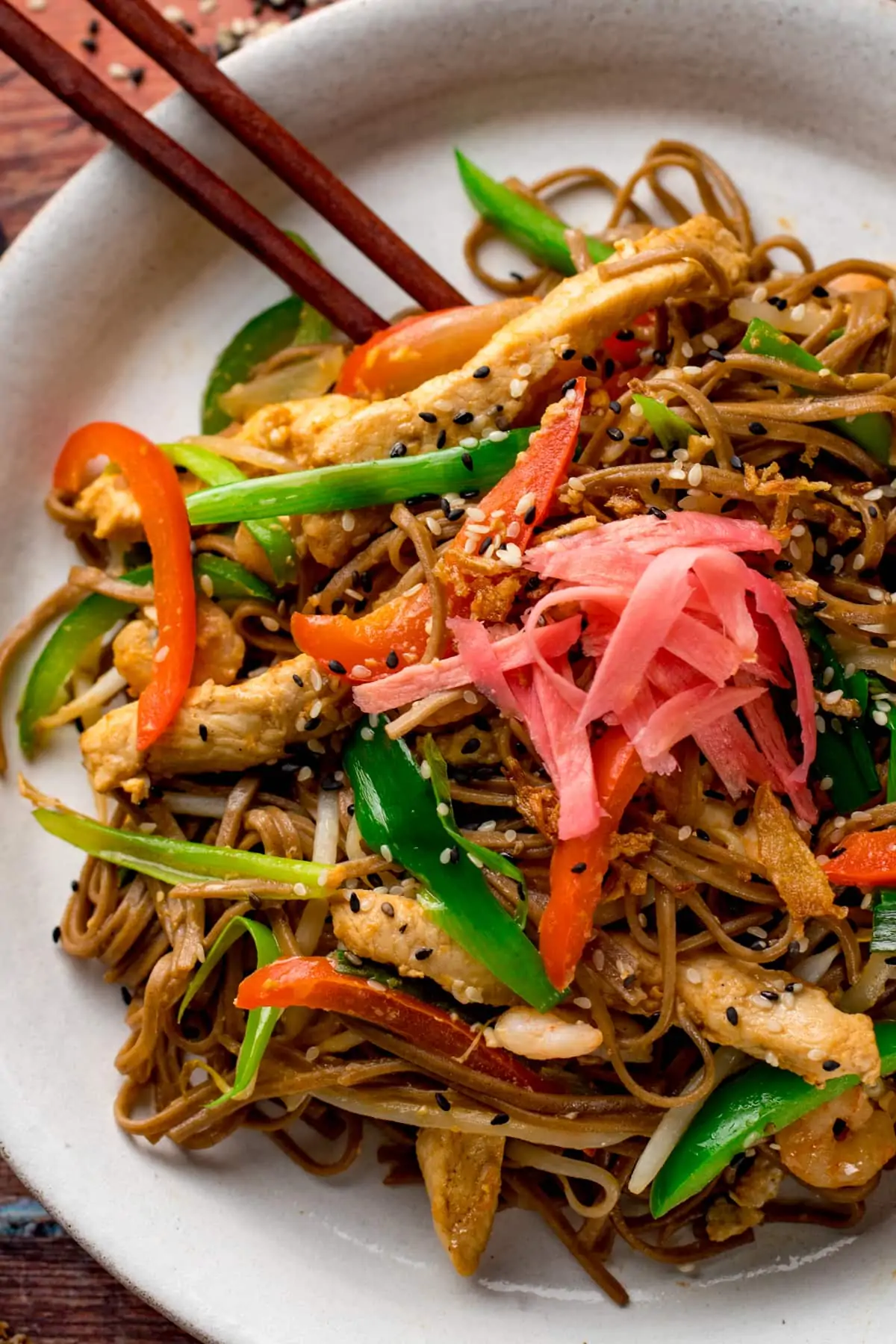 Close up of chicken yakisoba on a white plate with some chopsticks on the side