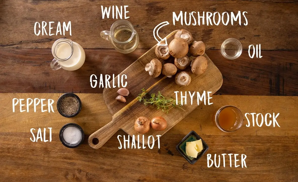 A wooden table with butter, mushrooms, thyme, shallots, garlic, wine, cream and salt and pepper on a wooden board