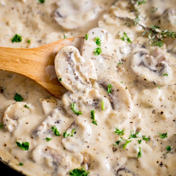 A square image of creamy mushroom sauce with a wooden spoon stirring it