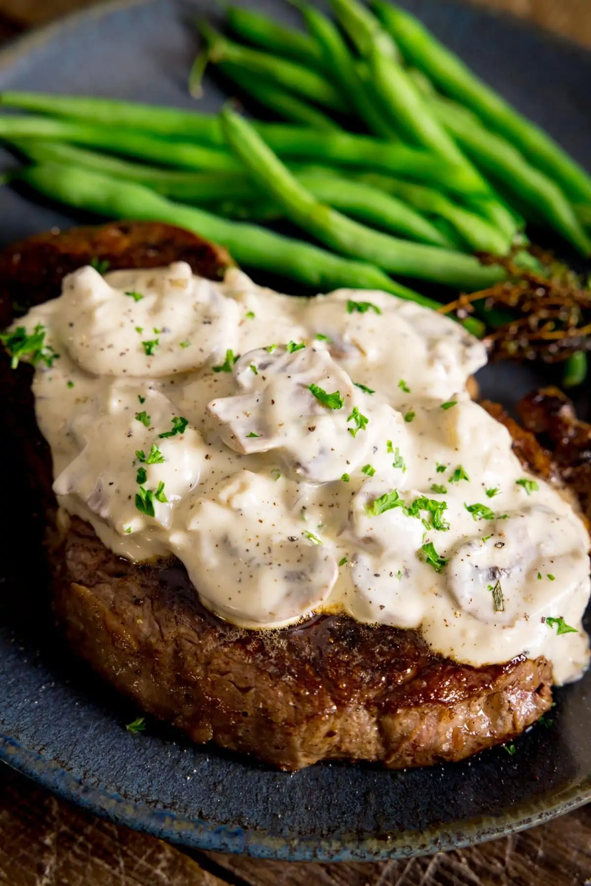 A blue plate with Creamy mushroom sauce on a cooked steak with green beans in the background
