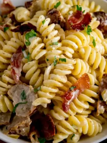 Overhead image of creamy pasta with sausage and bacon in a white bowl.