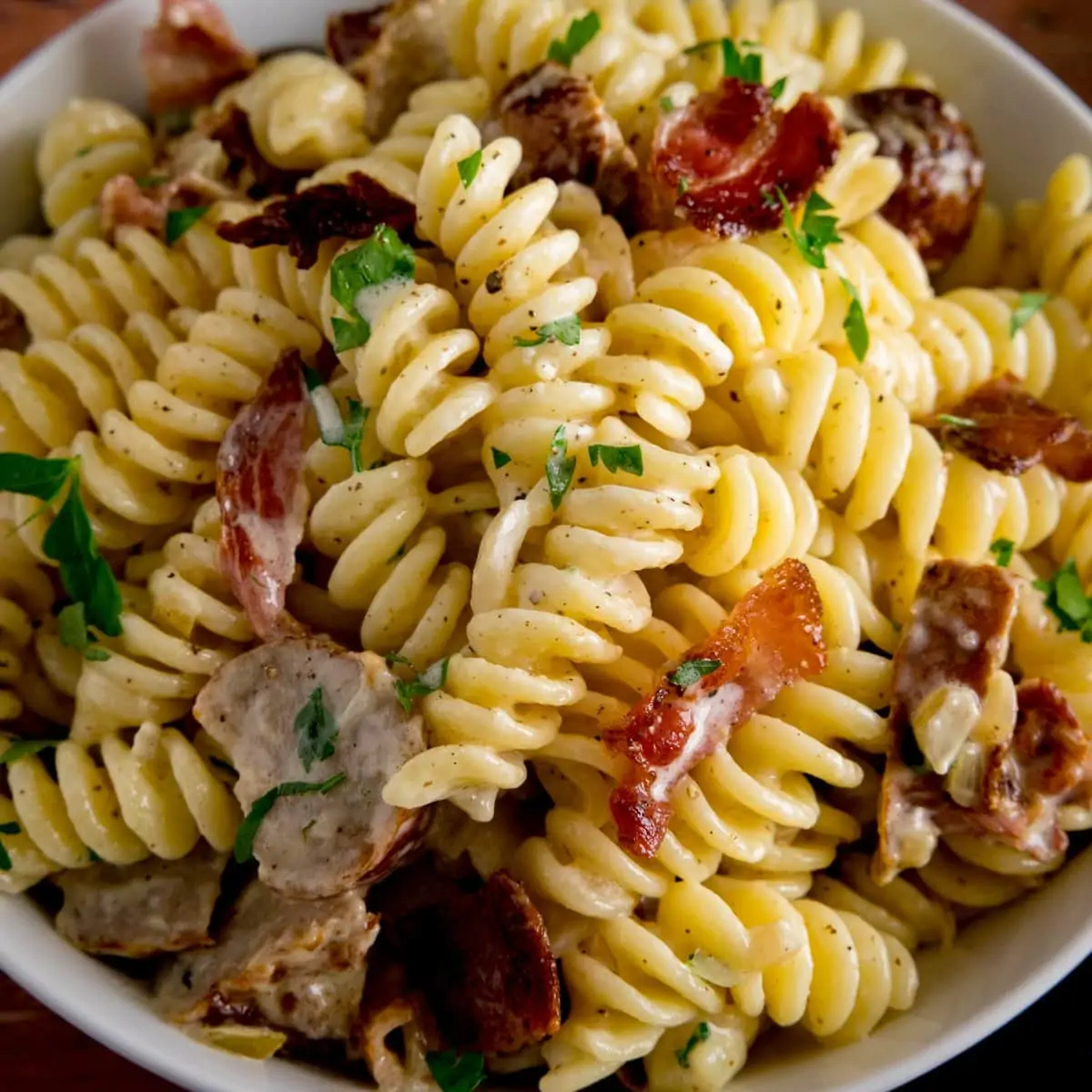 Overhead image of creamy pasta with sausage and bacon in a white bowl.