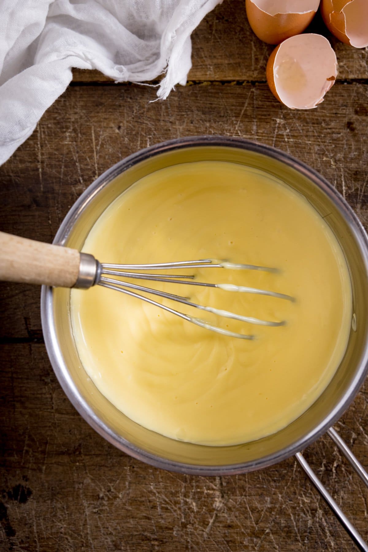 A close up of a big bowl of custard being whisked on a wooden table