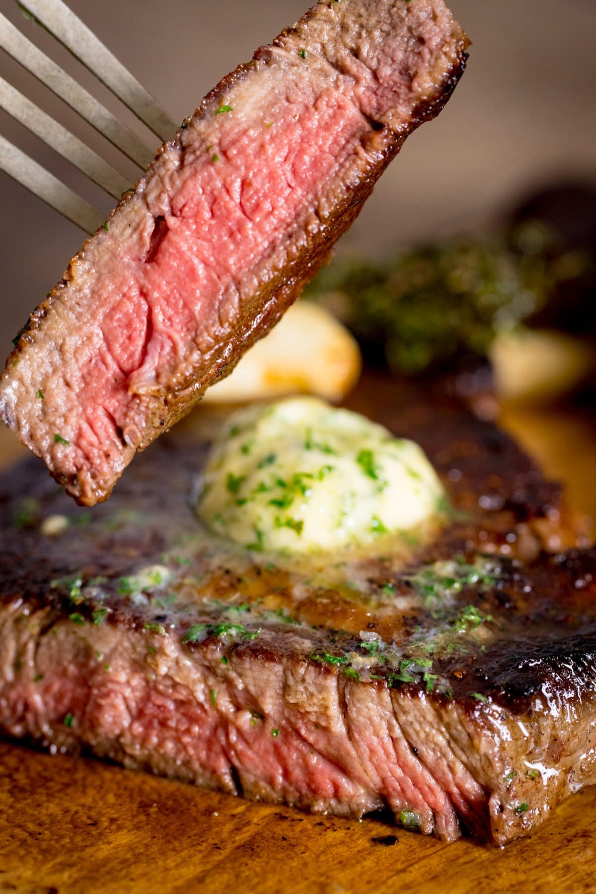 Cooked steak on a wooden board, topped with garlic butter. A slice has been taken from the steak and is being lifted by a fork