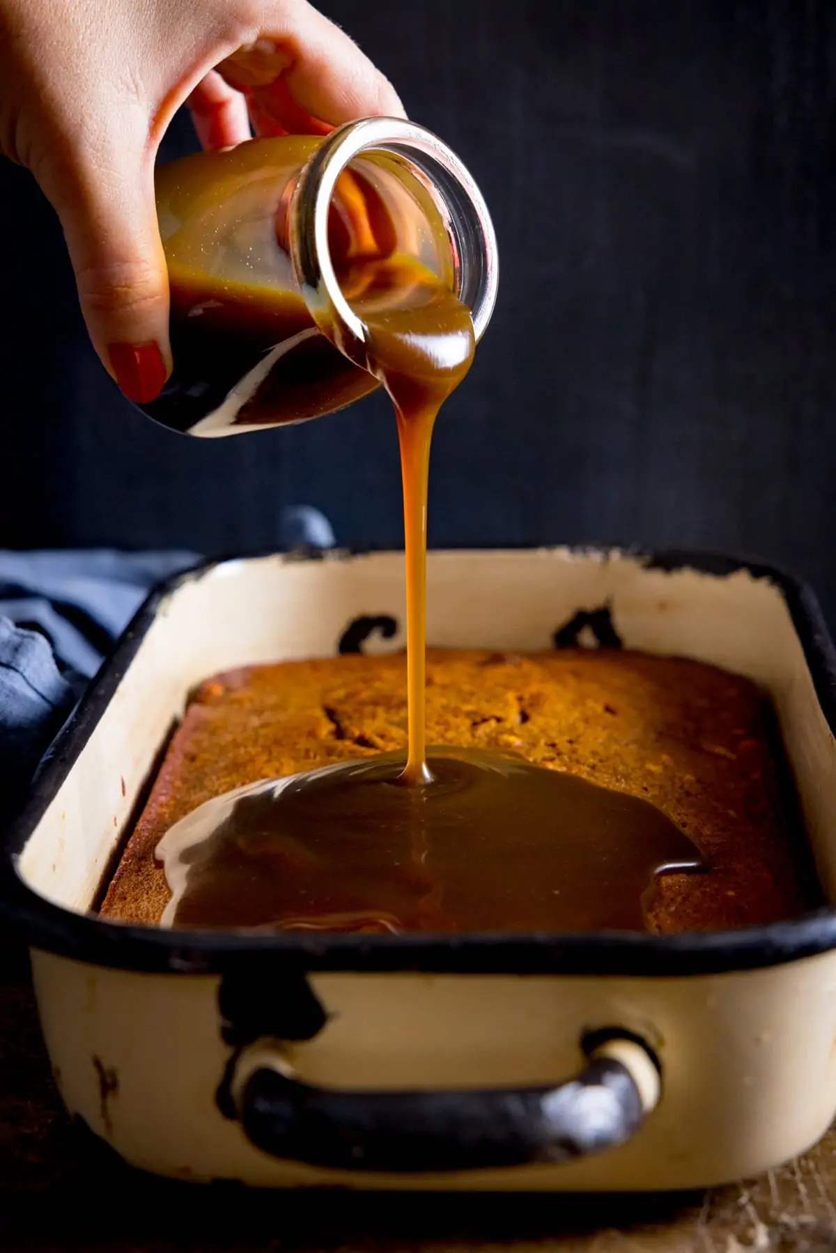 Toffee sauce being poured onto sticky toffee pudding cake
