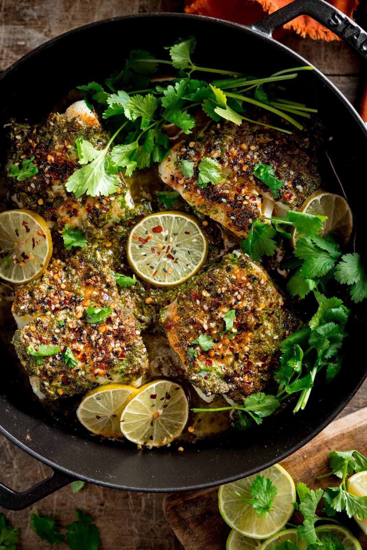 A pan full of coriander lime cod bake, garnished with parsley and slices of lemon on a table
