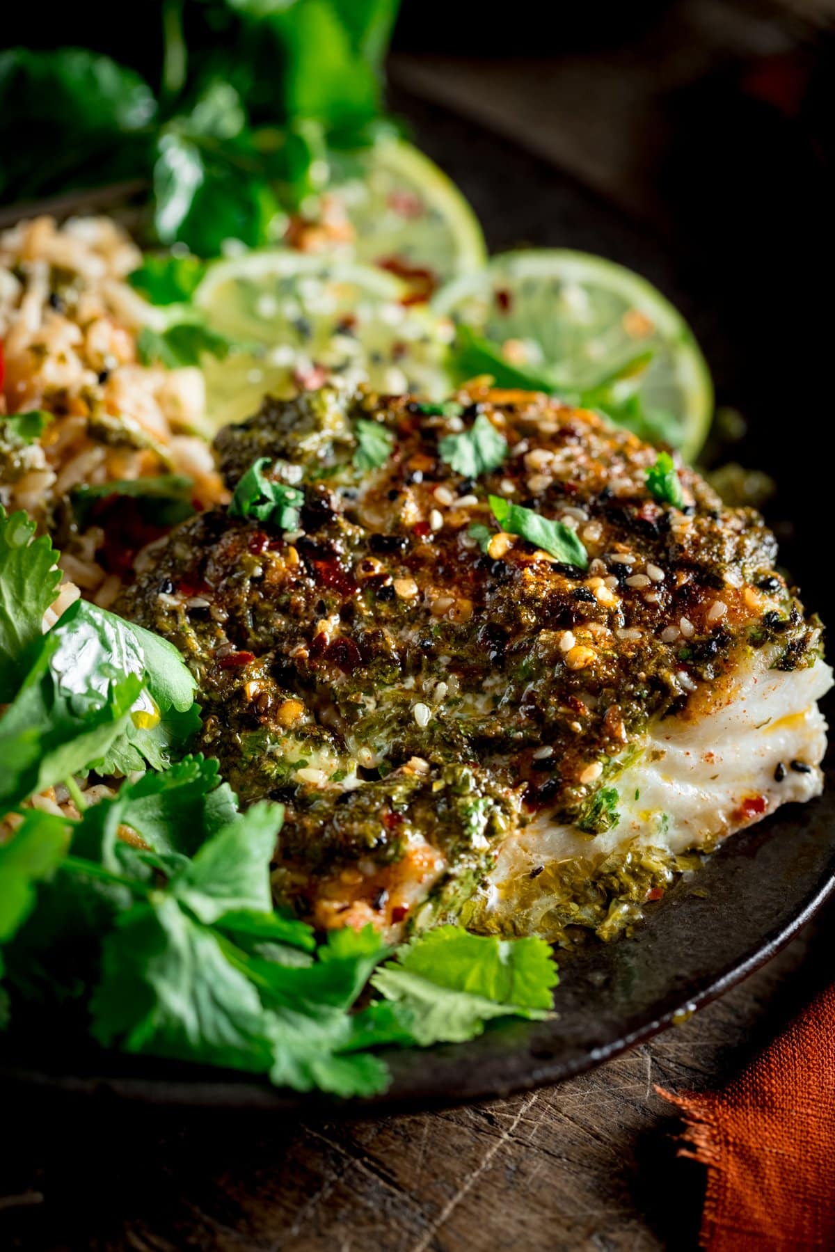 A black plate with coriander lime cod bake served on a bed of coriander and sliced lemon