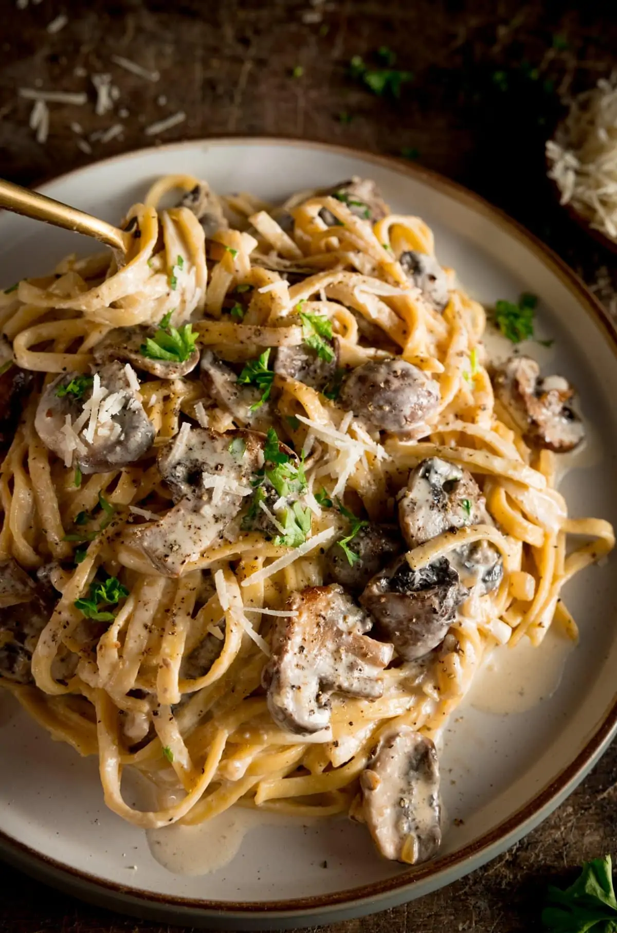 A white plate piled high with creamy mushroom pasta with a spoon sticking out