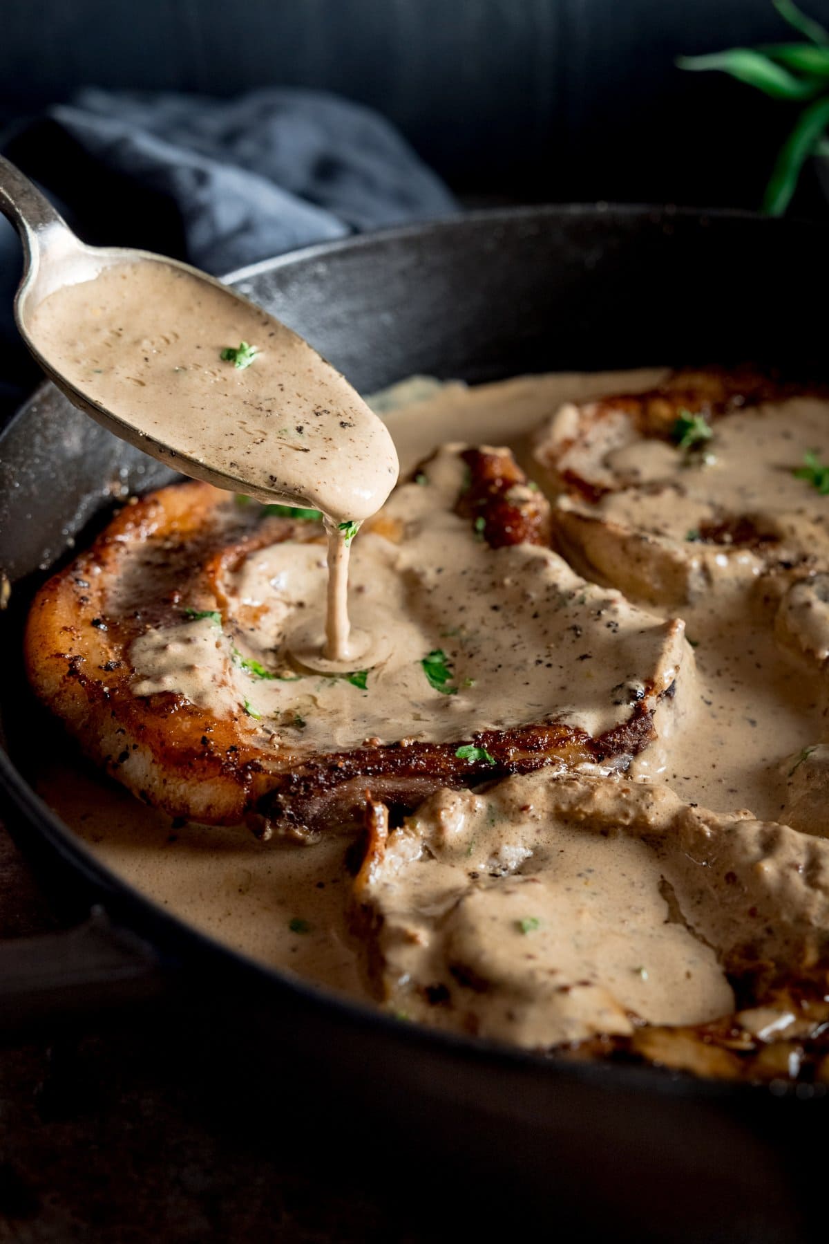 Cooked pork chops in a pan being drizzled with creamy mustard sauce