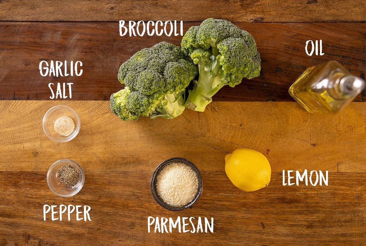 A wooden table with all of the ingredients laid out for roasted broccoli with garlic