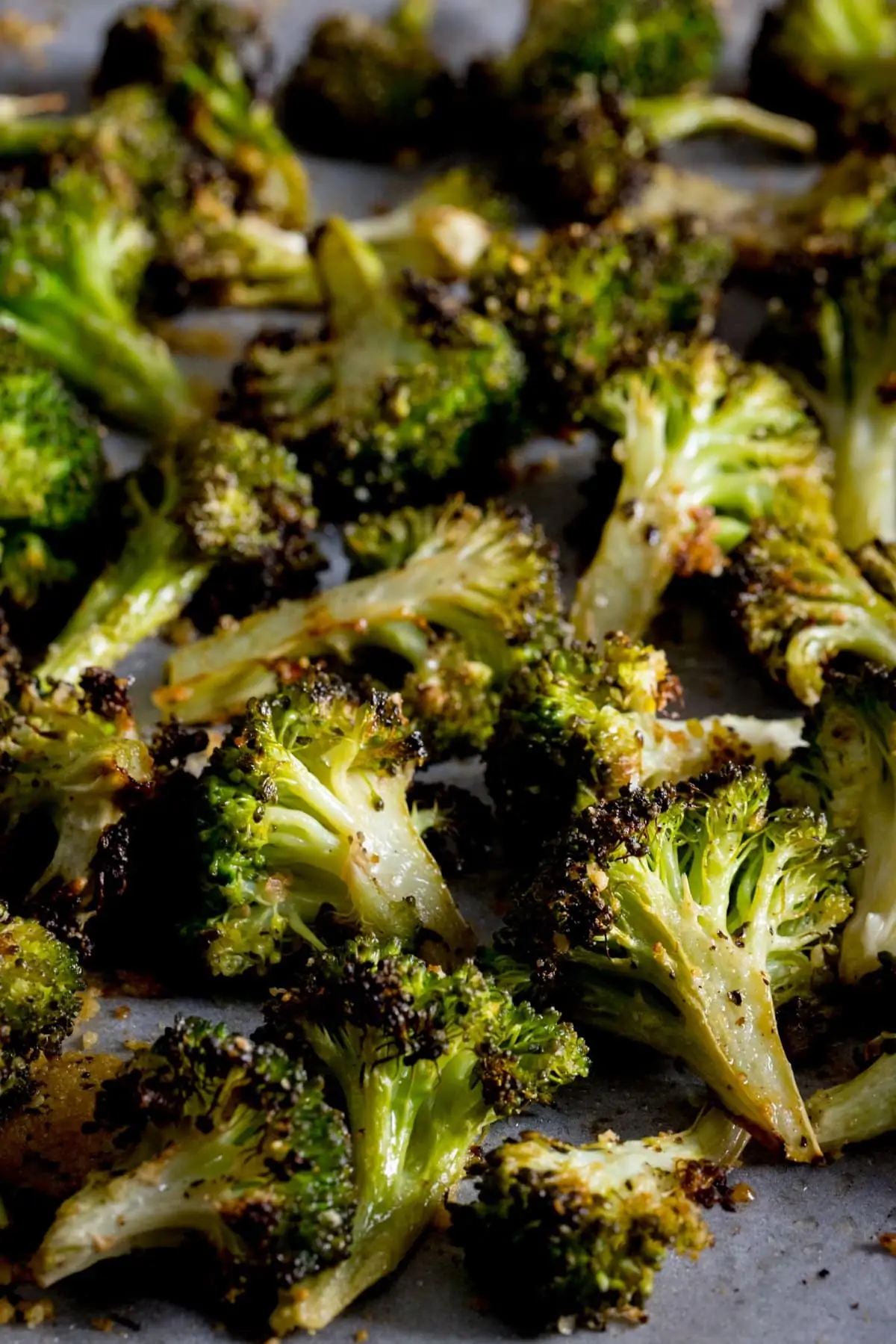A tall photo of roasted broccoli with garlic spread out on a white tray