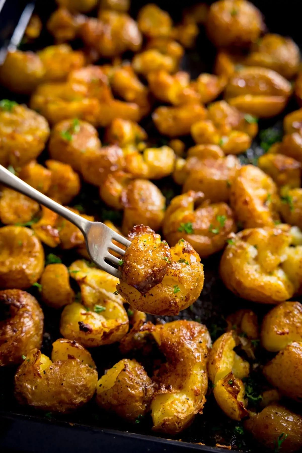 A fork digging into a big tray of crispy smashed potatoes