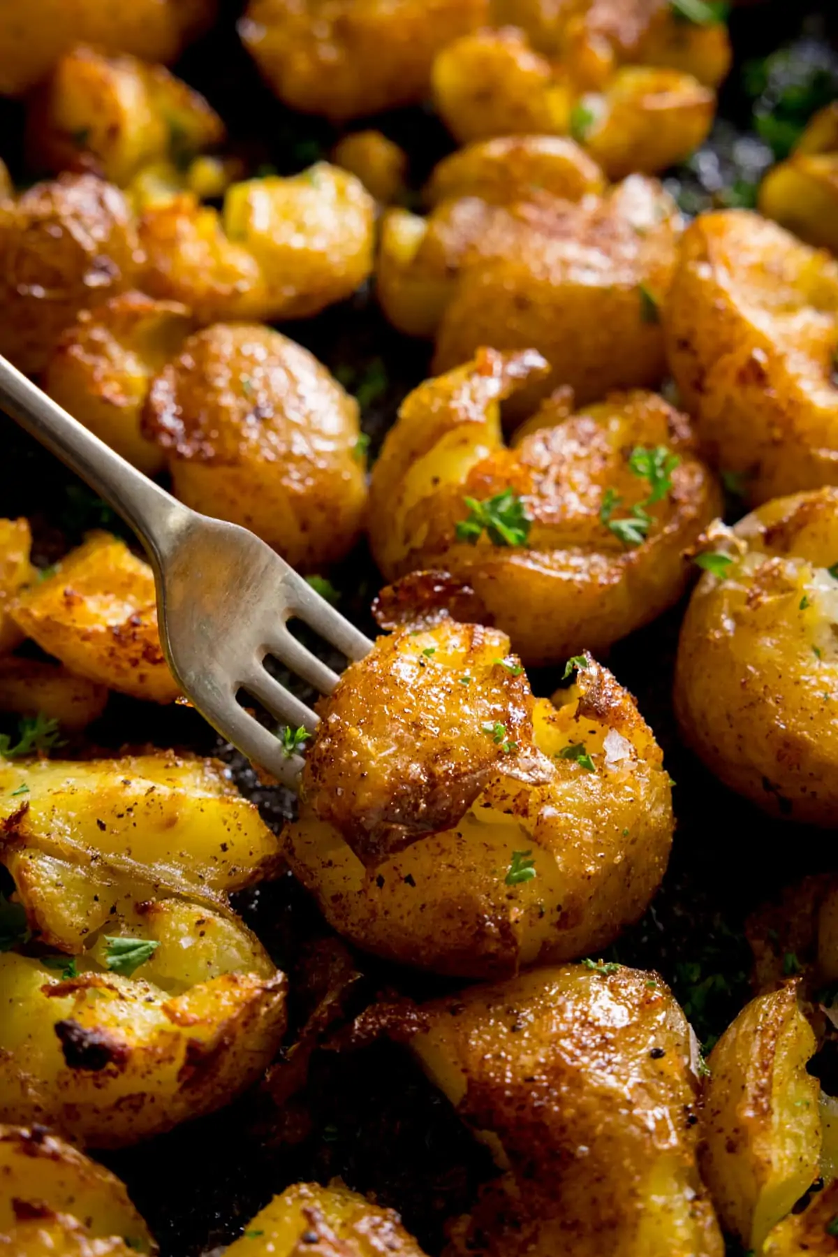 A plate of crispy smashed potatoes with a fork digging into a potato