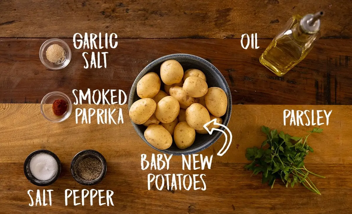 A wooden table with all of the ingredients for smashed potatoes laid out separately