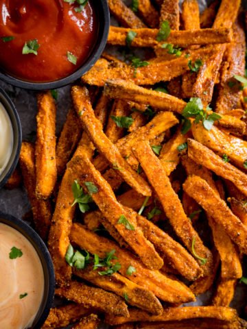 A tall image of cooked sweet potato fries, with three colourful dips alongside.