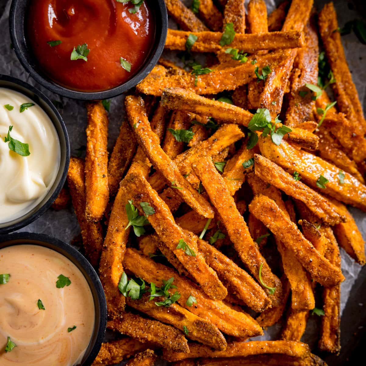 A tall image of cooked sweet potato fries, with three colourful dips alongside.