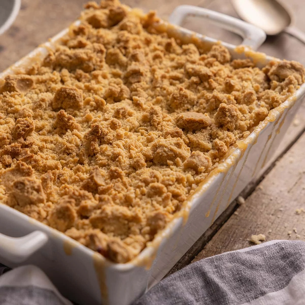 Photo of a white baking dish full of apple crumble on a rustic wooden table.