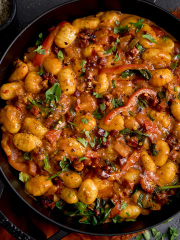 Square image of gnocchi and chorizo in harissa sauce in a black cast iron pan.