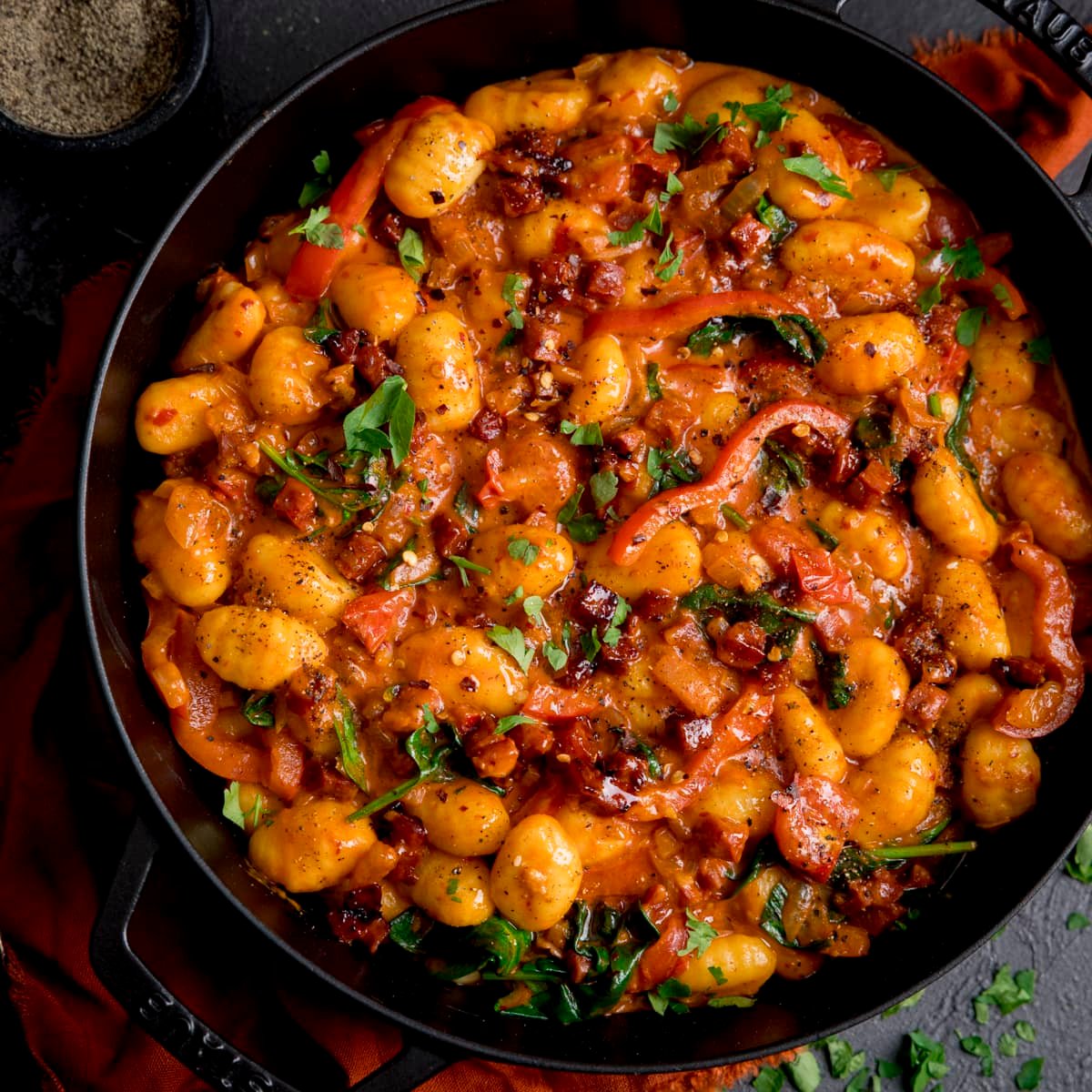 Square image of gnocchi and chorizo in harissa sauce in a black cast iron pan.