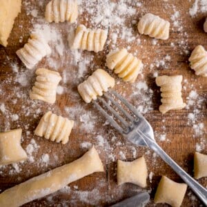 Gnocchi being cut and shaped on a wooden board. There is a fork in shot - used for rolling