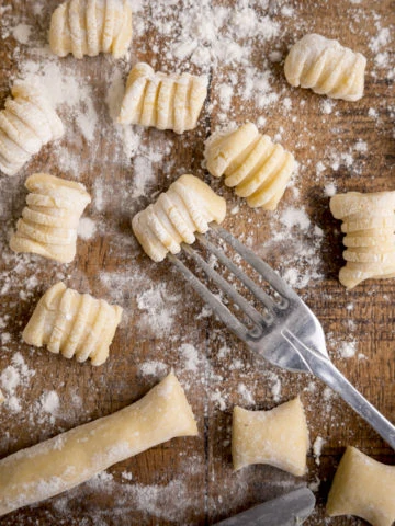 Gnocchi being cut and shaped on a wooden board. There is a fork in shot - used for rolling