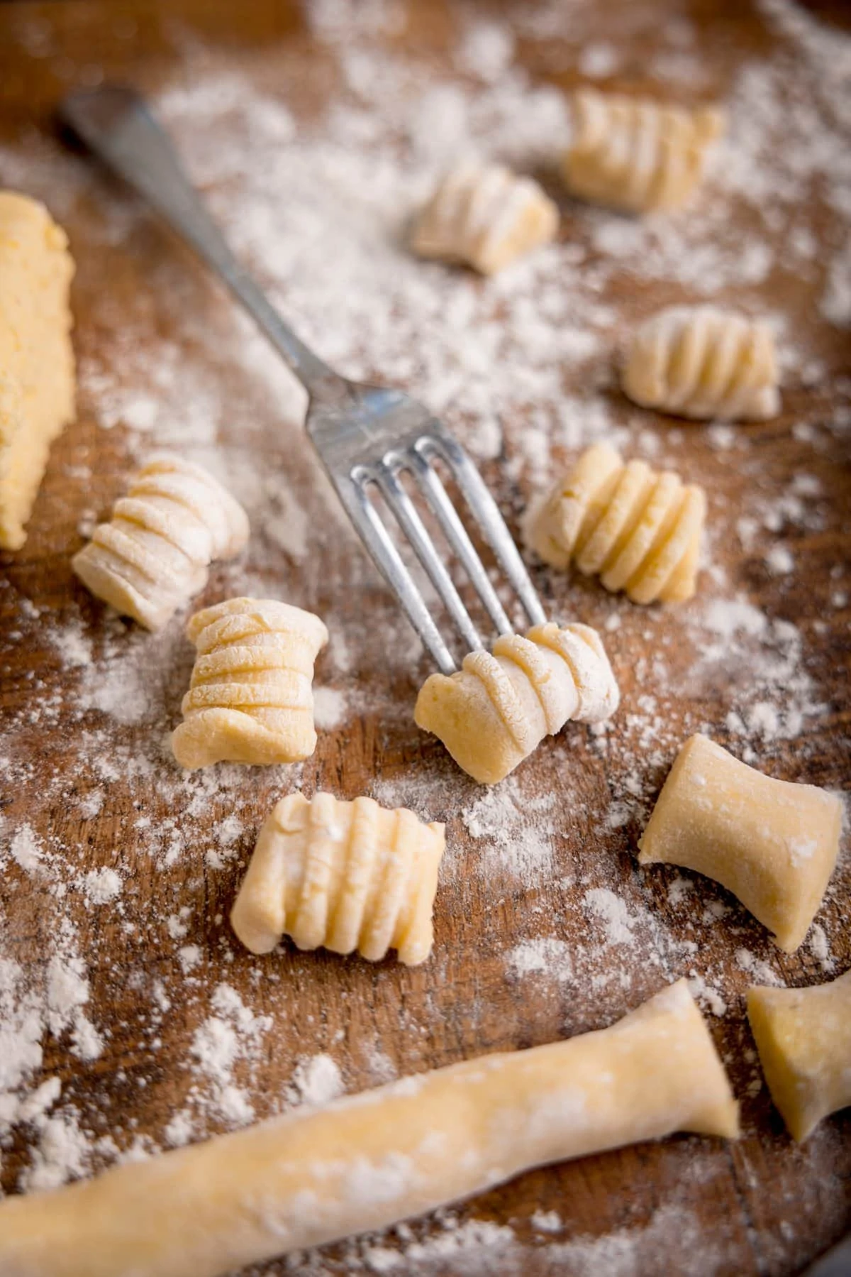 Gnocchi being shaped using the back of a fork on a floured board. There are pieces of gnocchi around the fork.