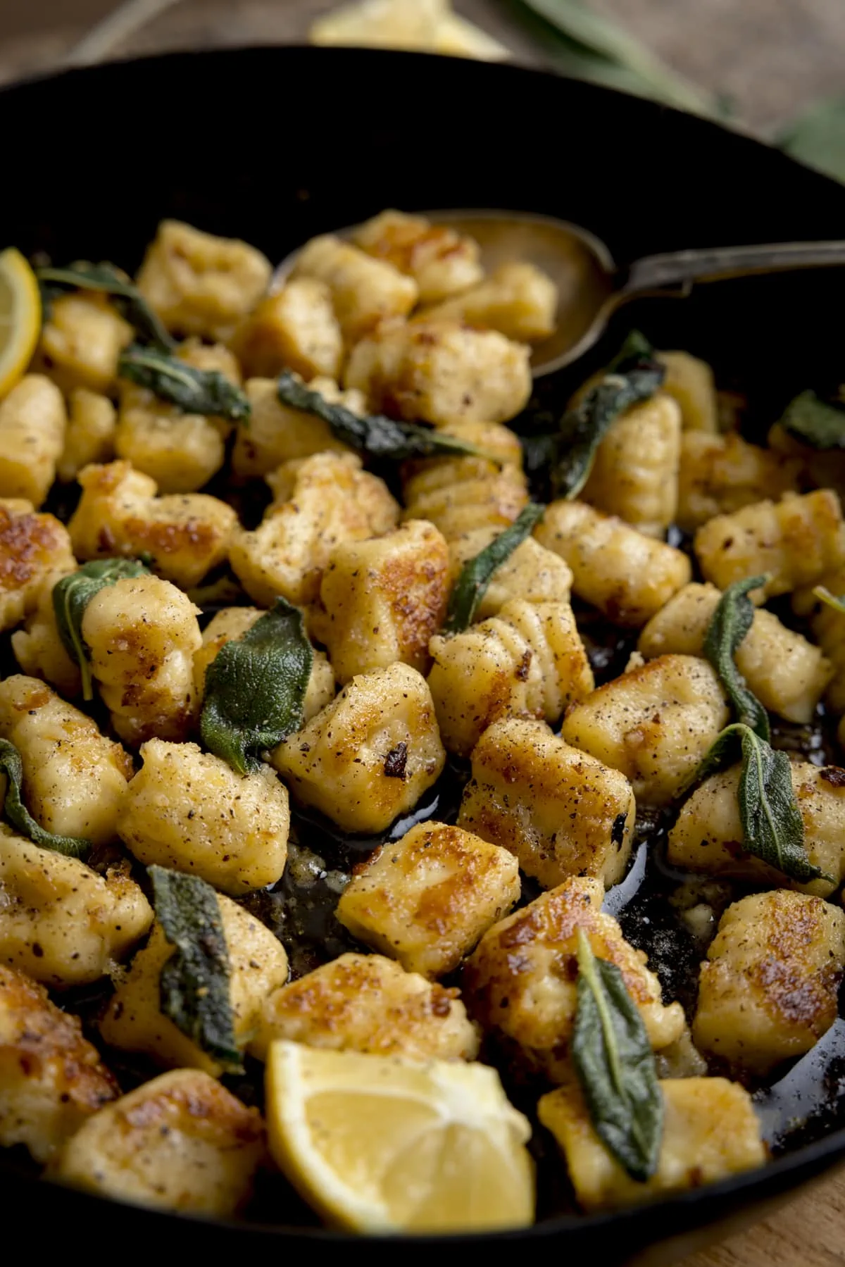 Pan fried gnocchi with brown butter and sage in a pan. There is a lemon wedge in the pan.