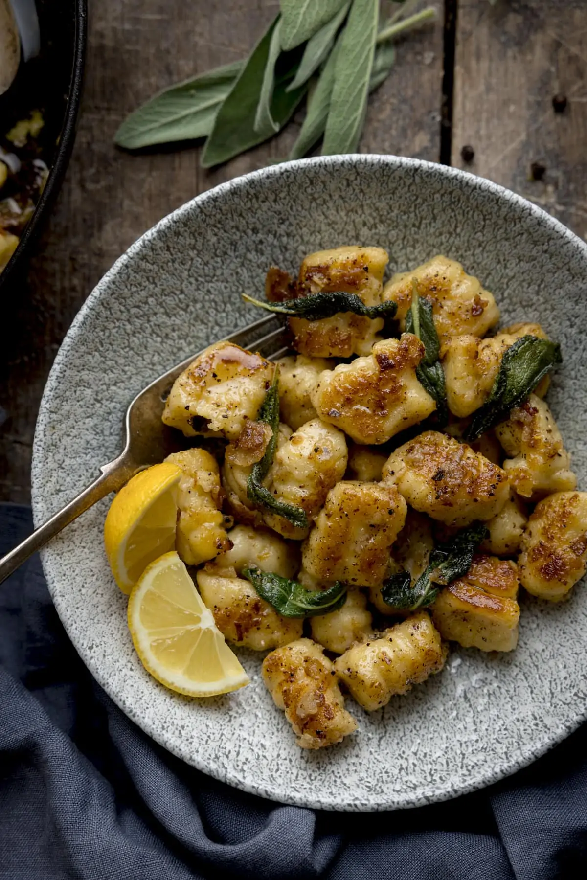 Gnocchi with brown butter and sage in a bowl. There are two lemon wedges and a fork in the bowl.