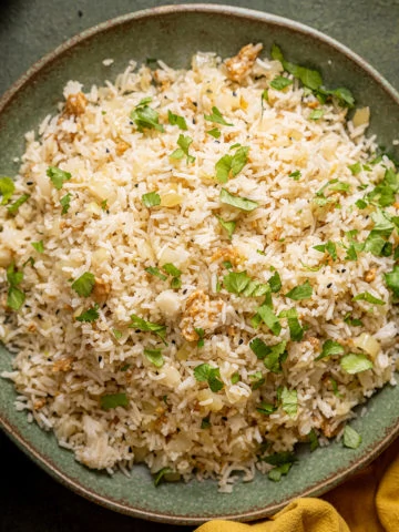 Onion Fried Rice on a green plate with a mustard coloured cloth in the bottom right hand corner.