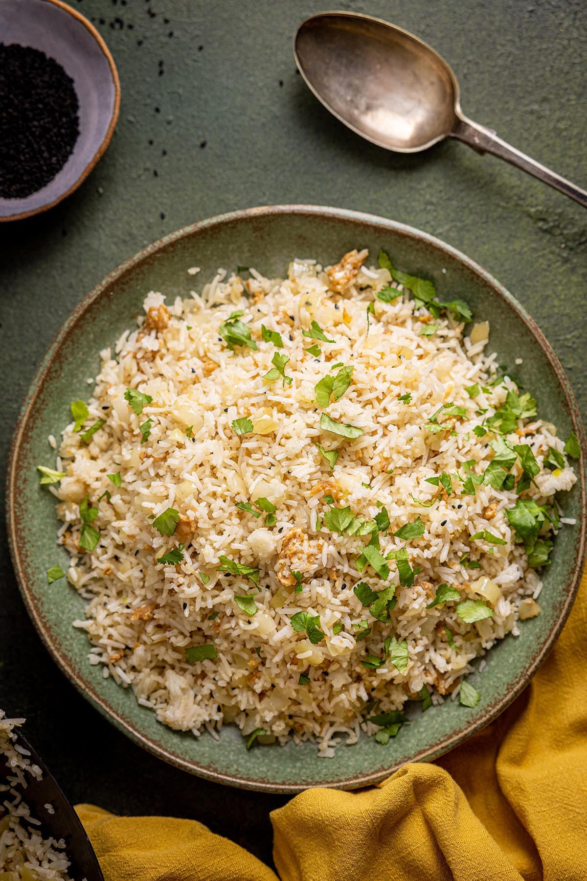 Gebratener Reis mit Zwiebeln auf einem grünen Teller, bestreut mit Koriander und einer Senfserviette in der unteren Ecke.