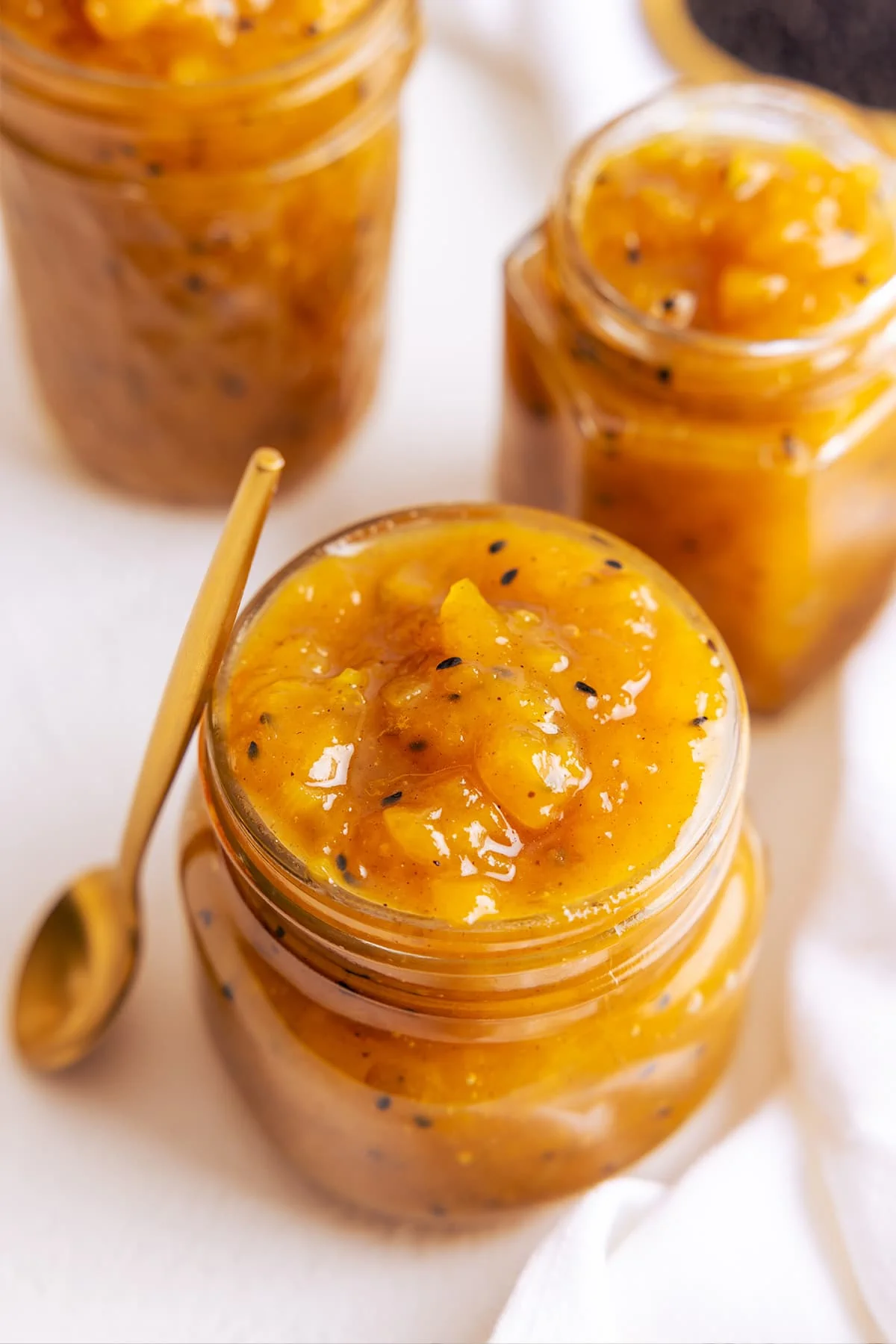 Close up picture of mango chutney in a glass jar with a brass spoon stood up next to the jar.