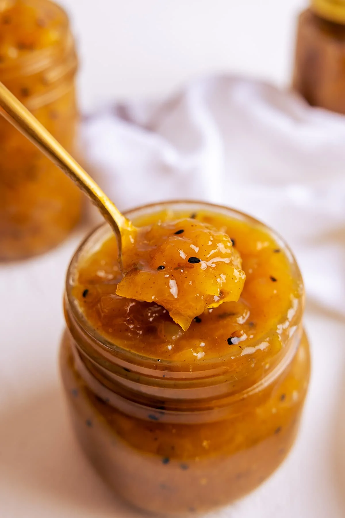 A brass spoon taking a spoon full of mango chutney out of a glass jar.