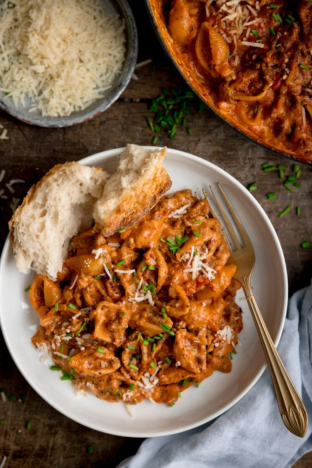 One pan pasta bolognese in a white bowl. There is a fork and a chunk of bread in the bowl.