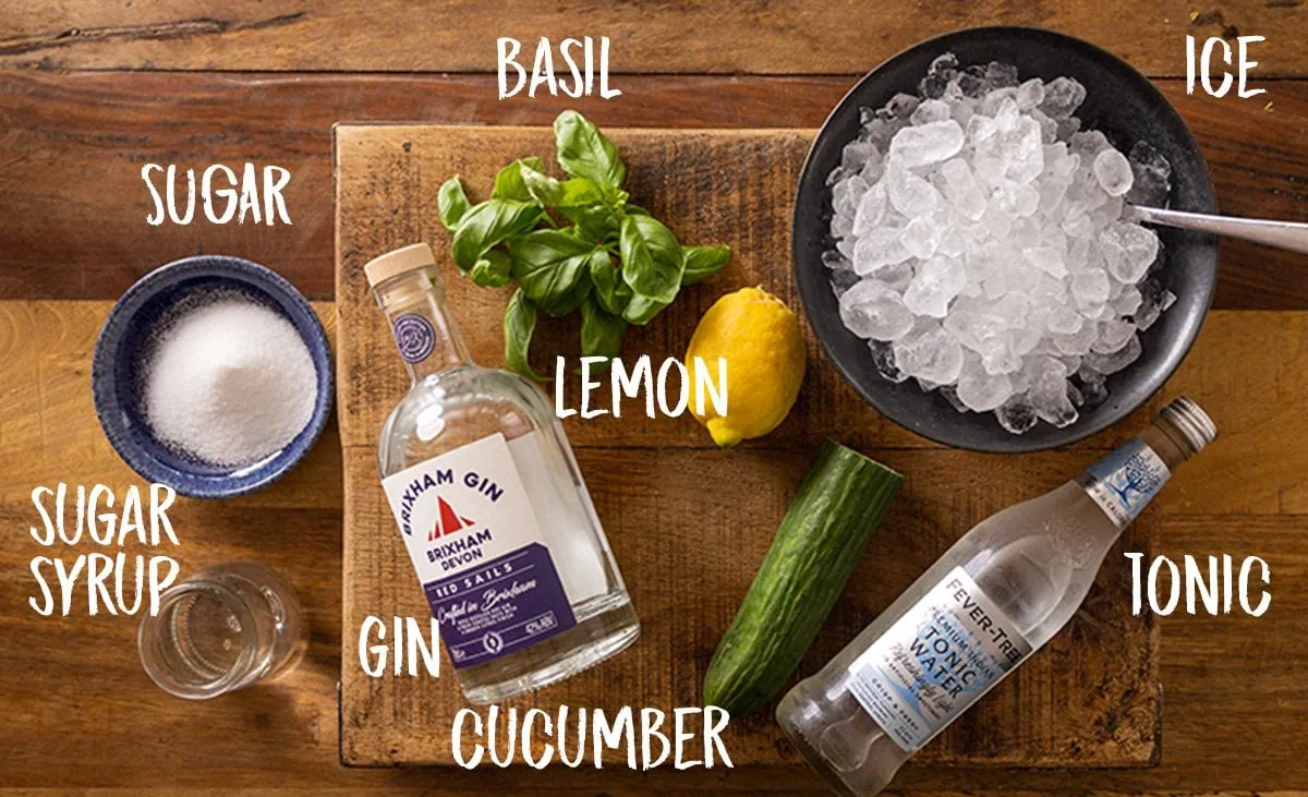Ingredients for gin and cucumber basil smash cocktail on a wooden table.
