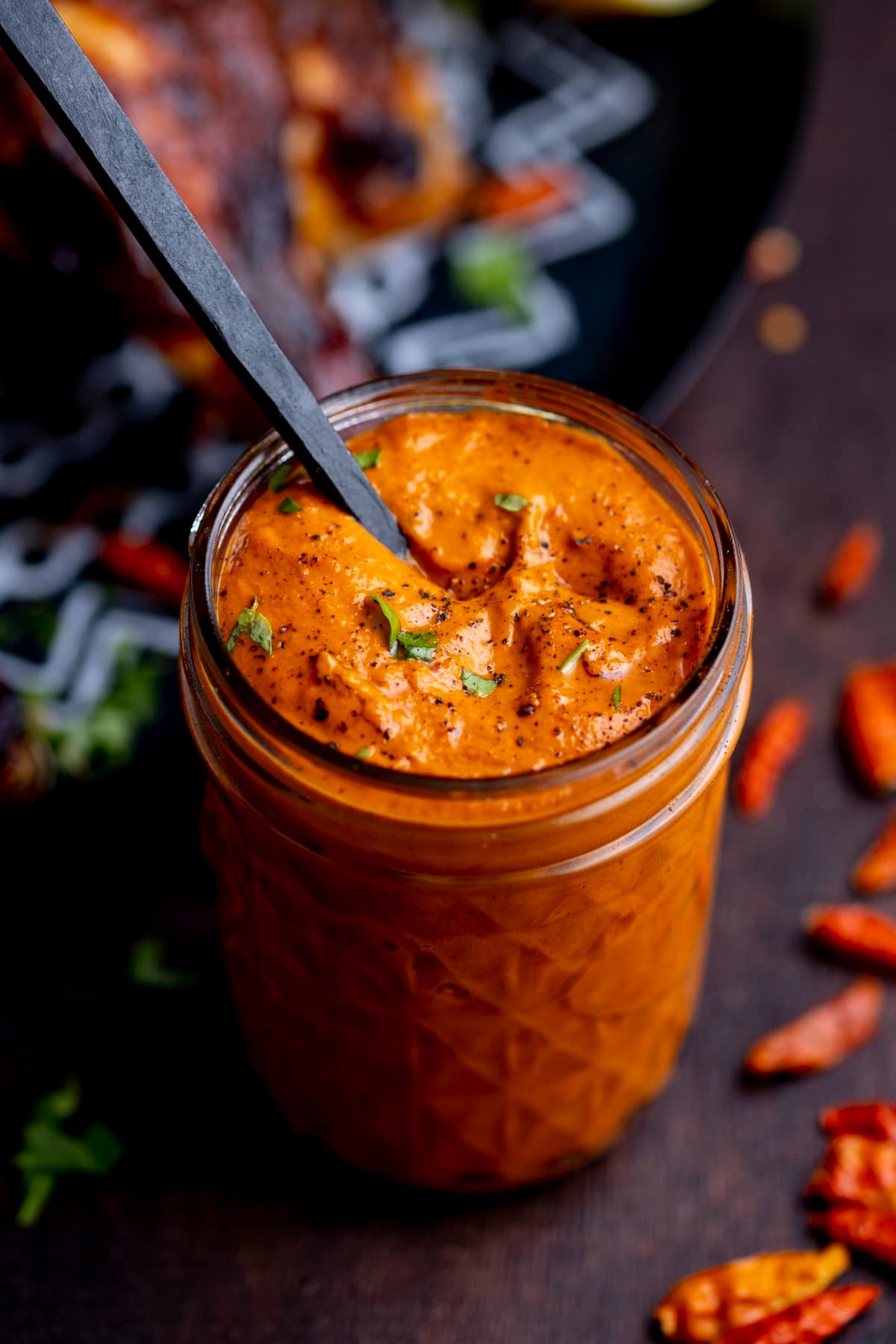 Homemade peri peri sauce in a glass jar with a black spoon sticking out of it.